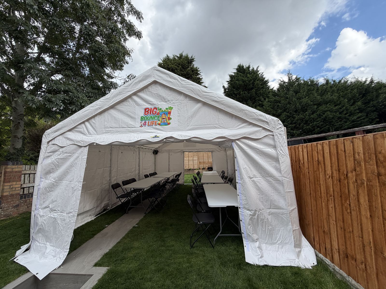 White 4m x 6m party marquee on a garden lawn beside a wooden fence, with tables set out inside