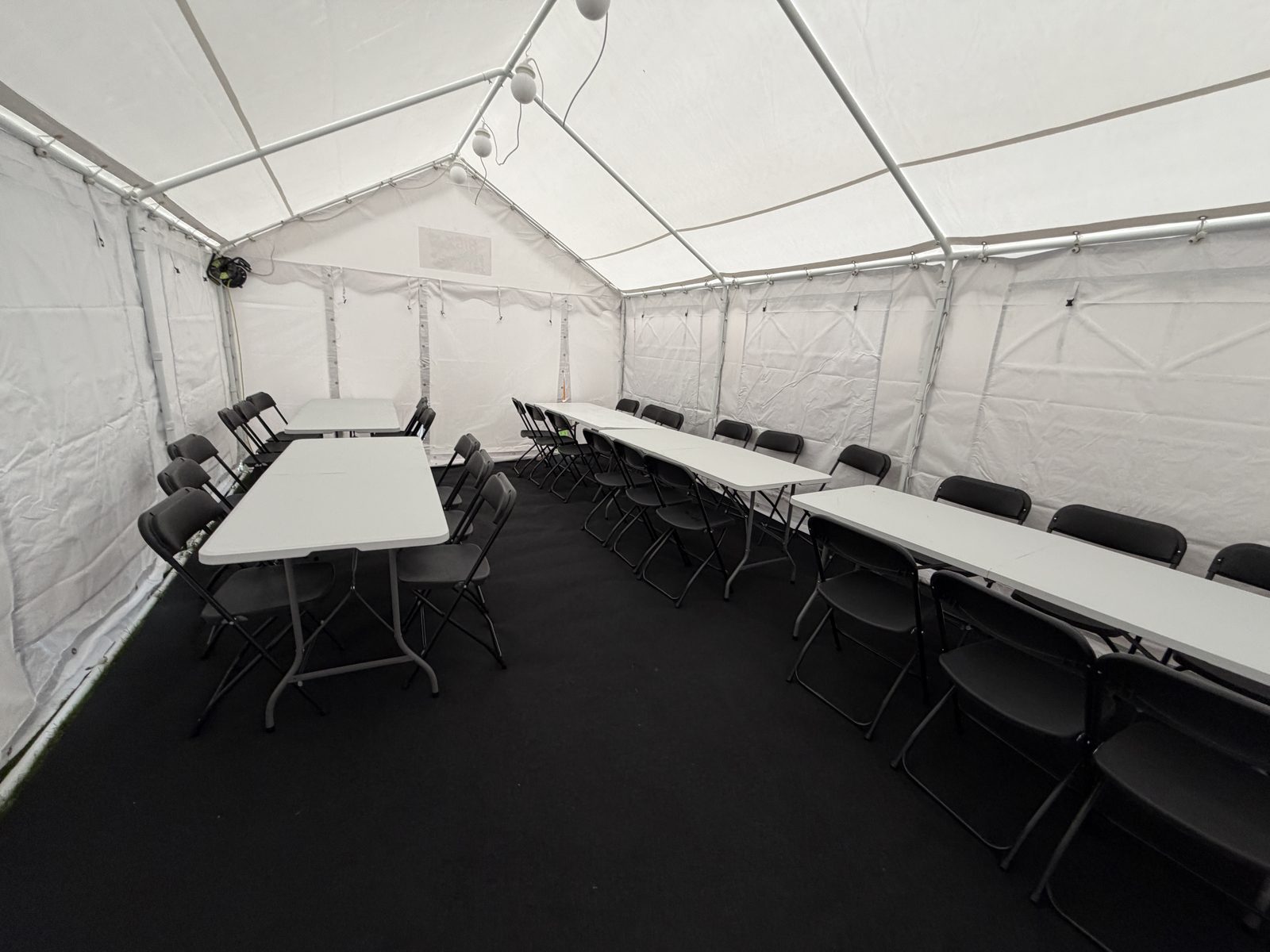 Inside the marquee: folding tables and black chairs laid out on dark flooring under a white roof