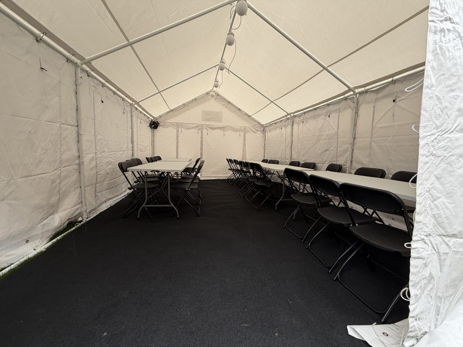 Marquee interior with black floor covering, tables along both sides and white walls