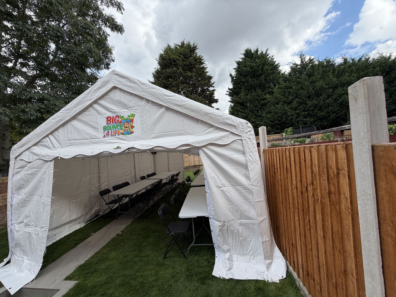 Marquee with both front doors open, showing tables inside, on a garden lawn next to a fence