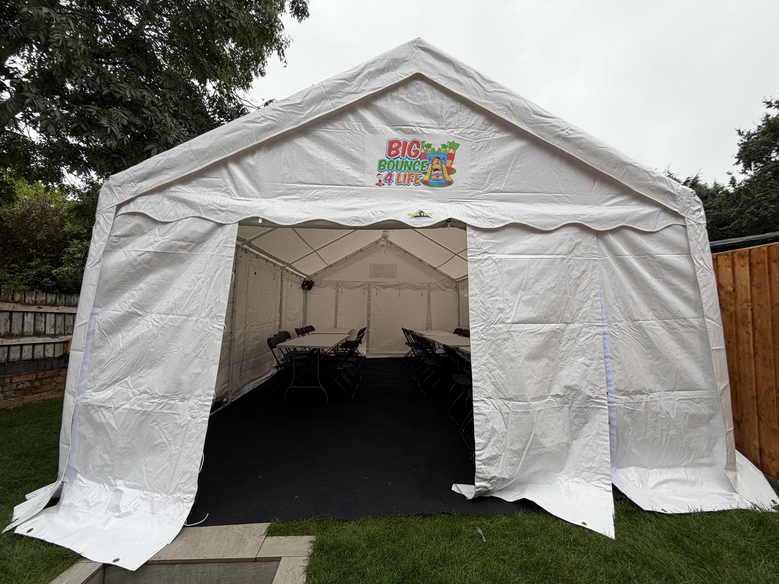 Front view of the white party marquee with dark flooring and tables set up inside