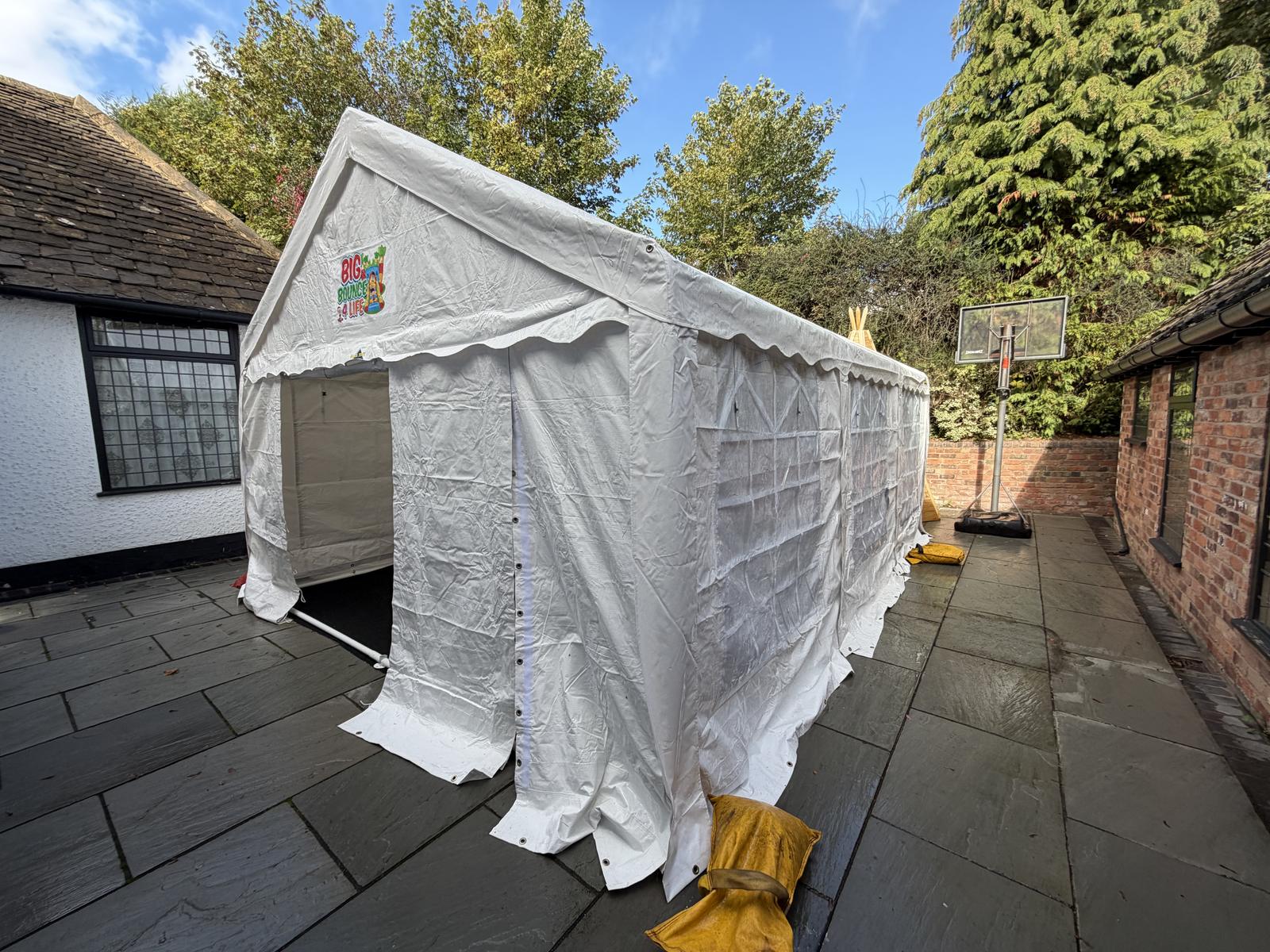 White marquee set up on a paved patio yard beside a house and tall trees
