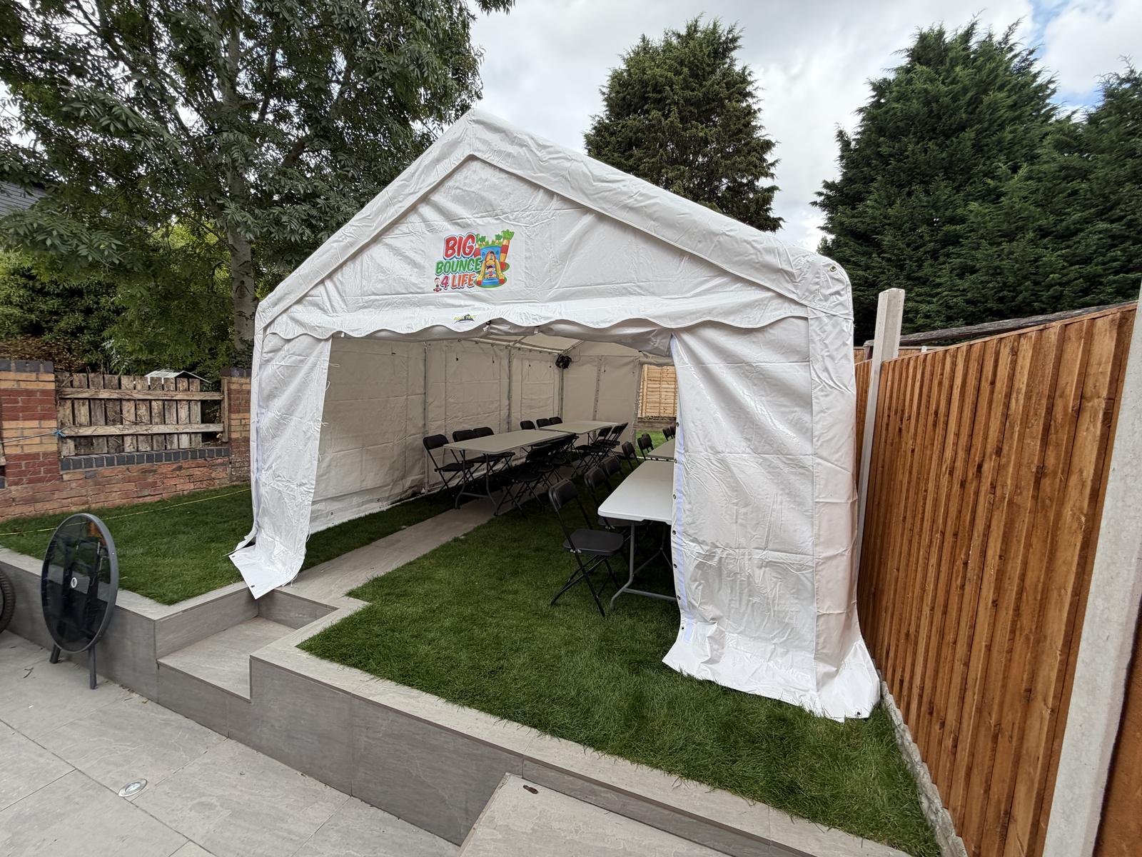 Marquee on a garden lawn seen from the patio step, with trees and a fence around it