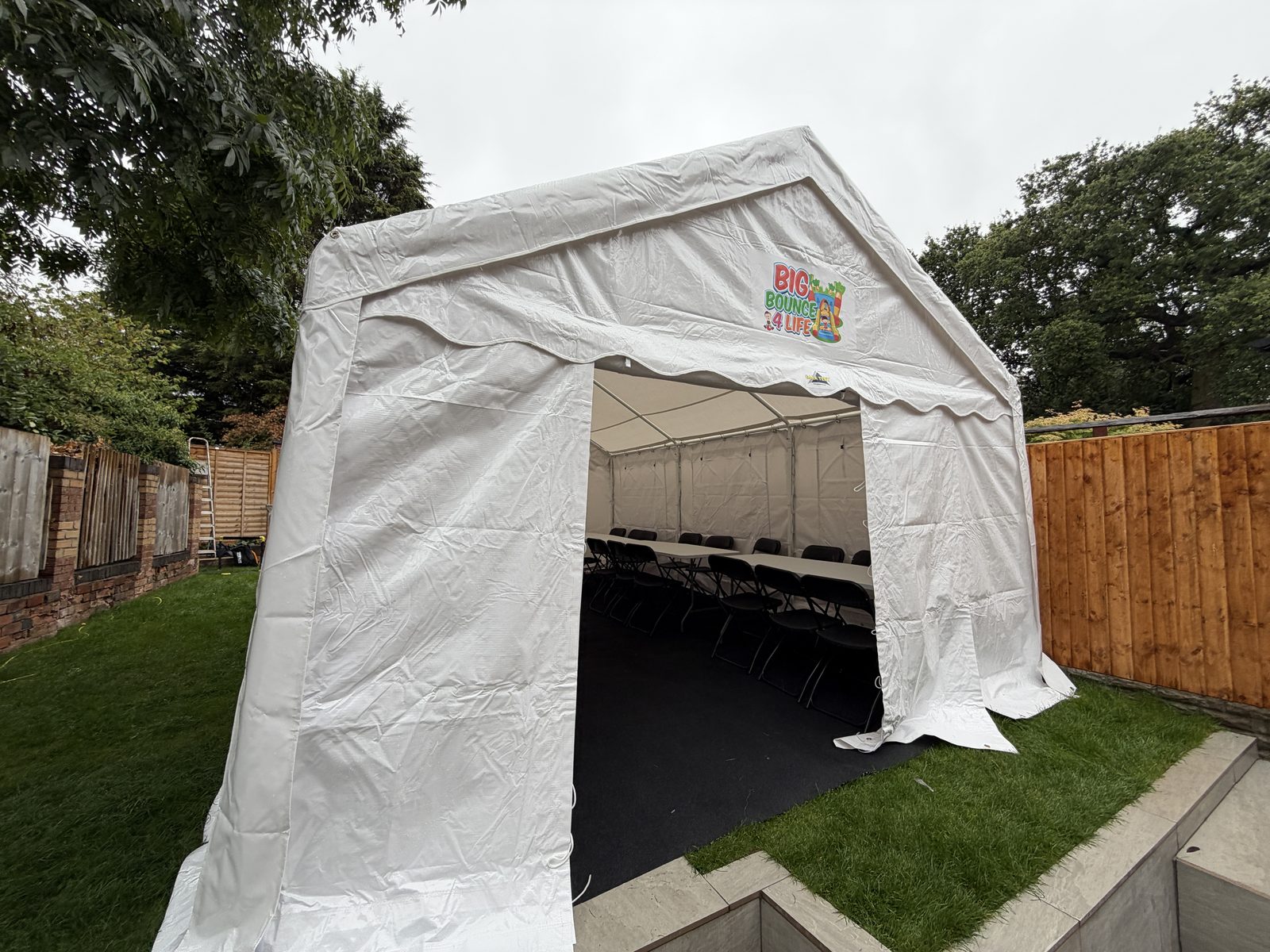 Front of the marquee with tables inside, set on a lawn with tall trees behind
